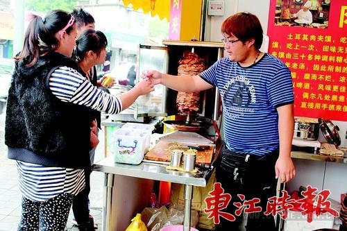 姜伟龙（右）把做好的肉夹馍递给顾客。 《东江时报》记者香金群 摄
